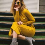 Stylish woman in yellow dress and sunglasses posing on steps. Modern fashion portrait.