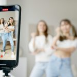 Two women dance in front of a smartphone camera, recording content indoors.